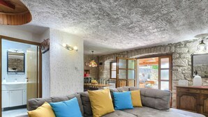 Una sala de estar acogedora con un sofá seccional, una mesita de centro con una planta, y una cocina visible a través de una puerta abierta.