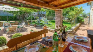 Un espacio para comer al aire libre con mesas y sillas de madera, rodeado de follaje y paredes de piedra.