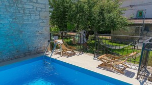 Una piscina con pared de piedra, sillas de descanso de madera y una hamaca.