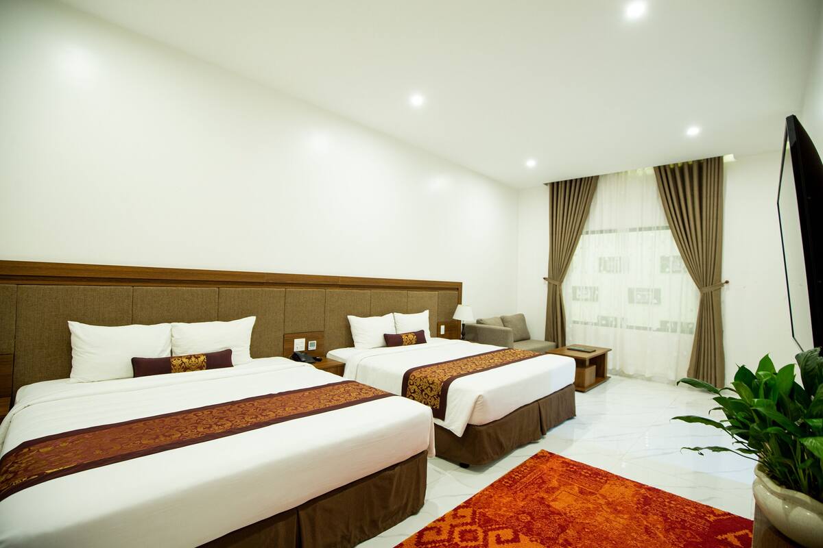 A hotel room with two beds, a sofa, a TV, and a potted plant.