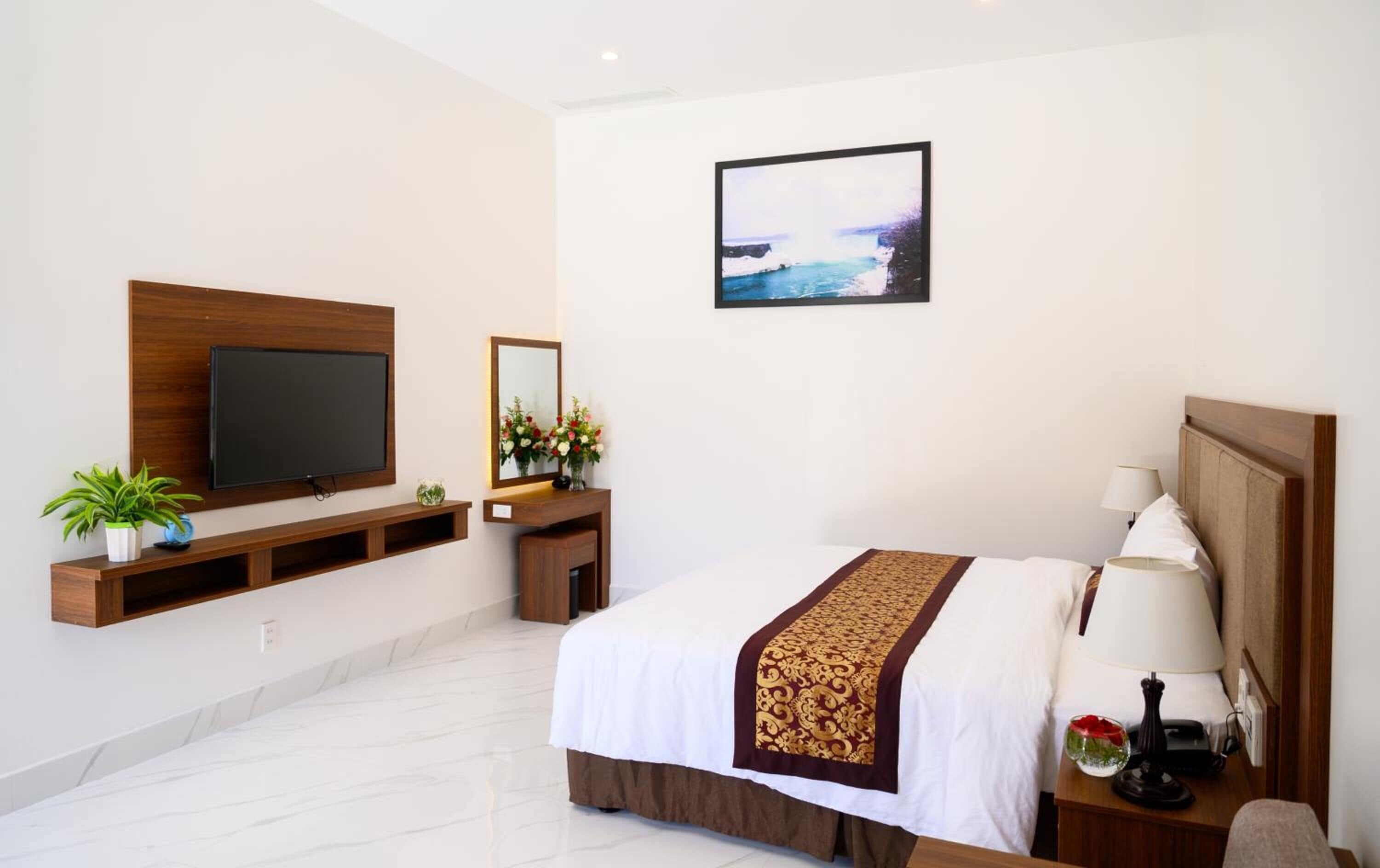A hotel room with a bed, a TV, a mirror, a desk, and a wall-mounted picture.