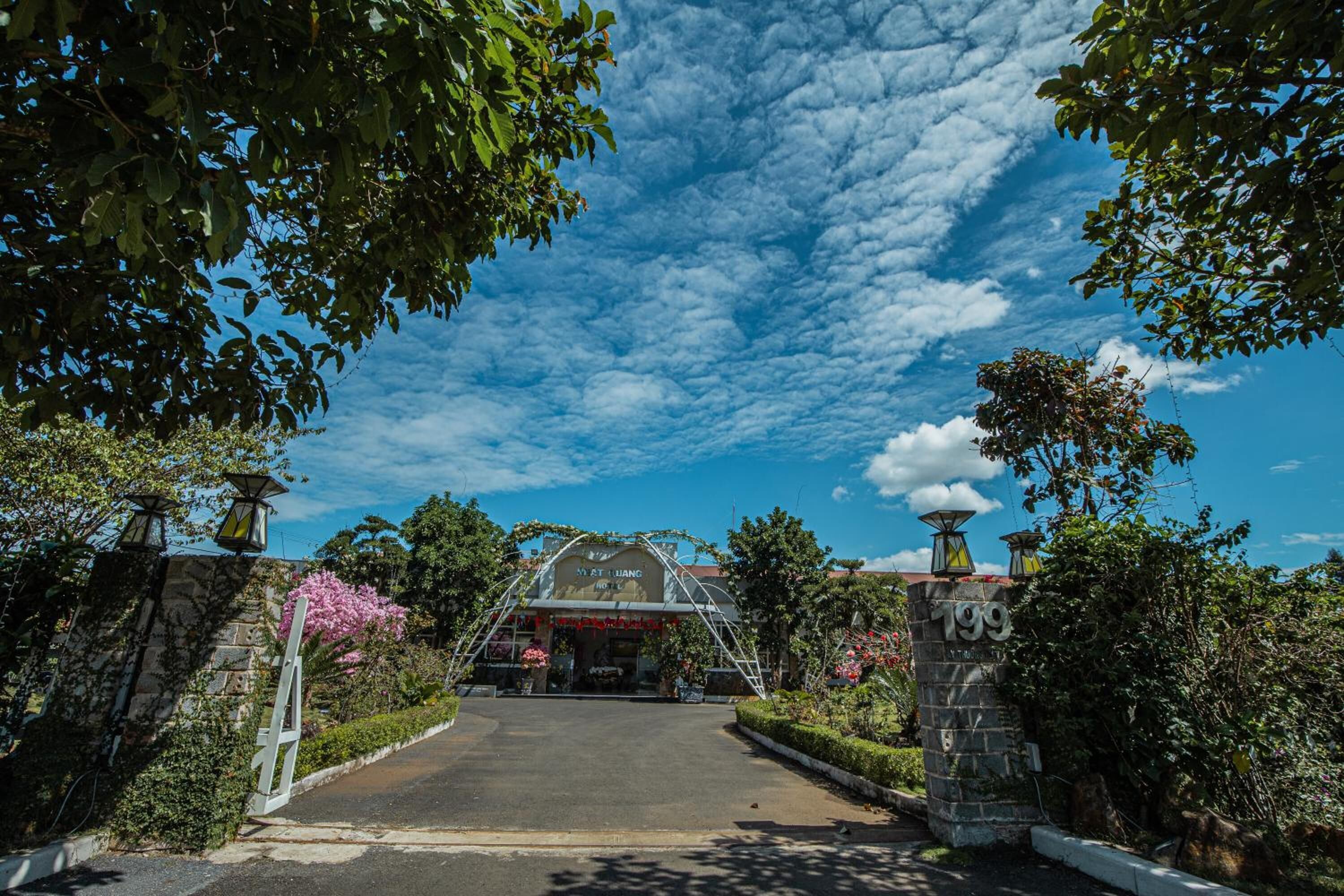 L’entrée d’un hôtel, avec une allée couverte, des murs en pierre et un ciel d’un bleu limpide.