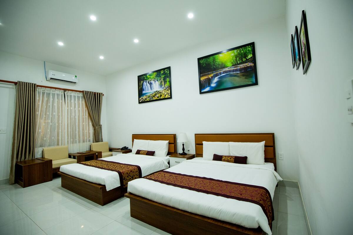 A hotel room with two beds, a sofa, a nightstand, and a window with curtains.