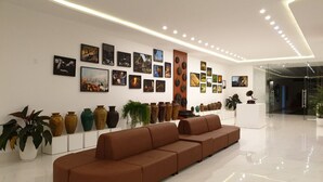 A modern lobby with a long brown sectional sofa, a row of decorative vases, and a wall adorned with framed artwork. - Nhat Quang Hotel (1 Bao Loc)