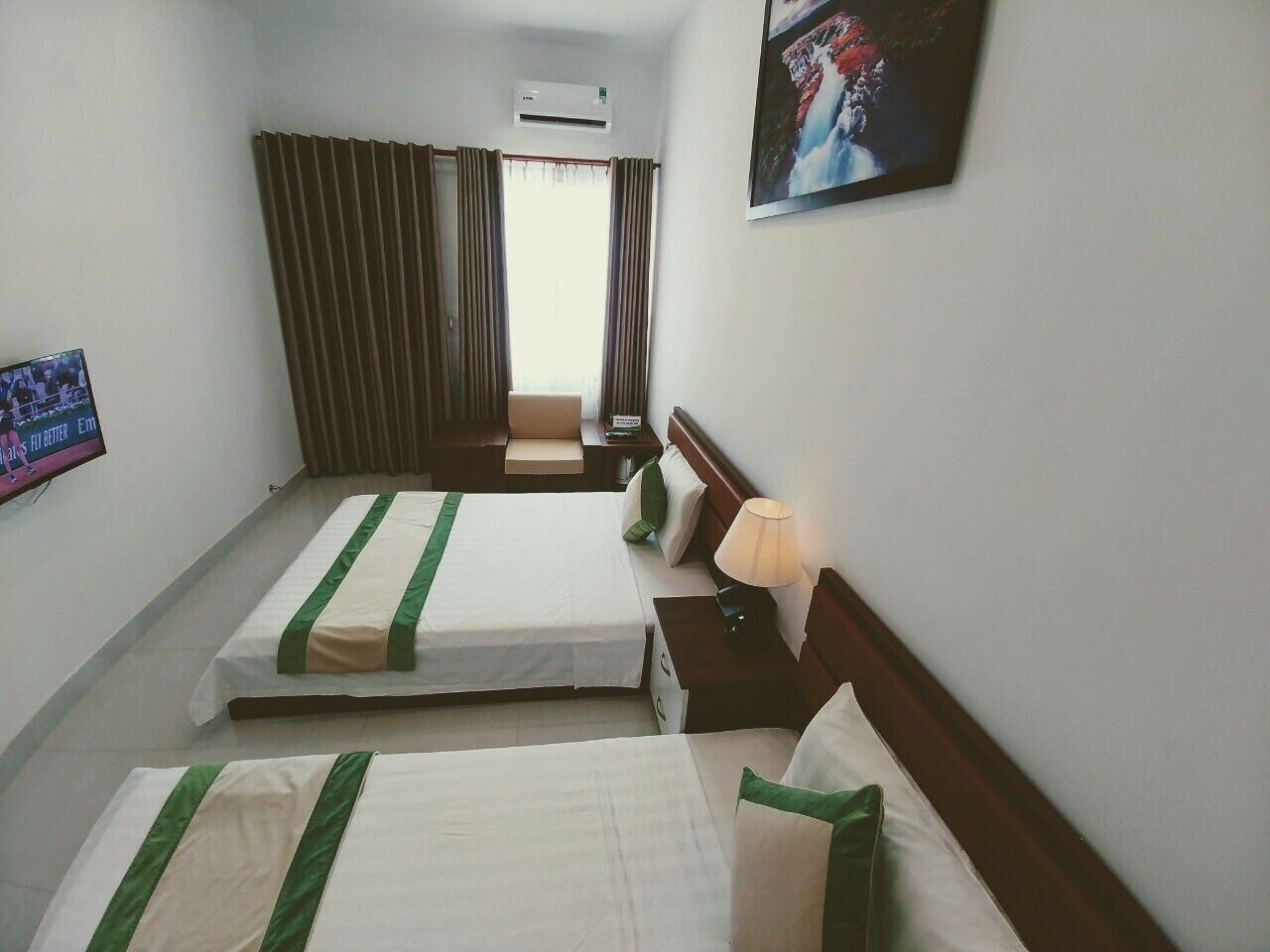 A hotel room with two beds, a TV, a painting, and a window with curtains.
