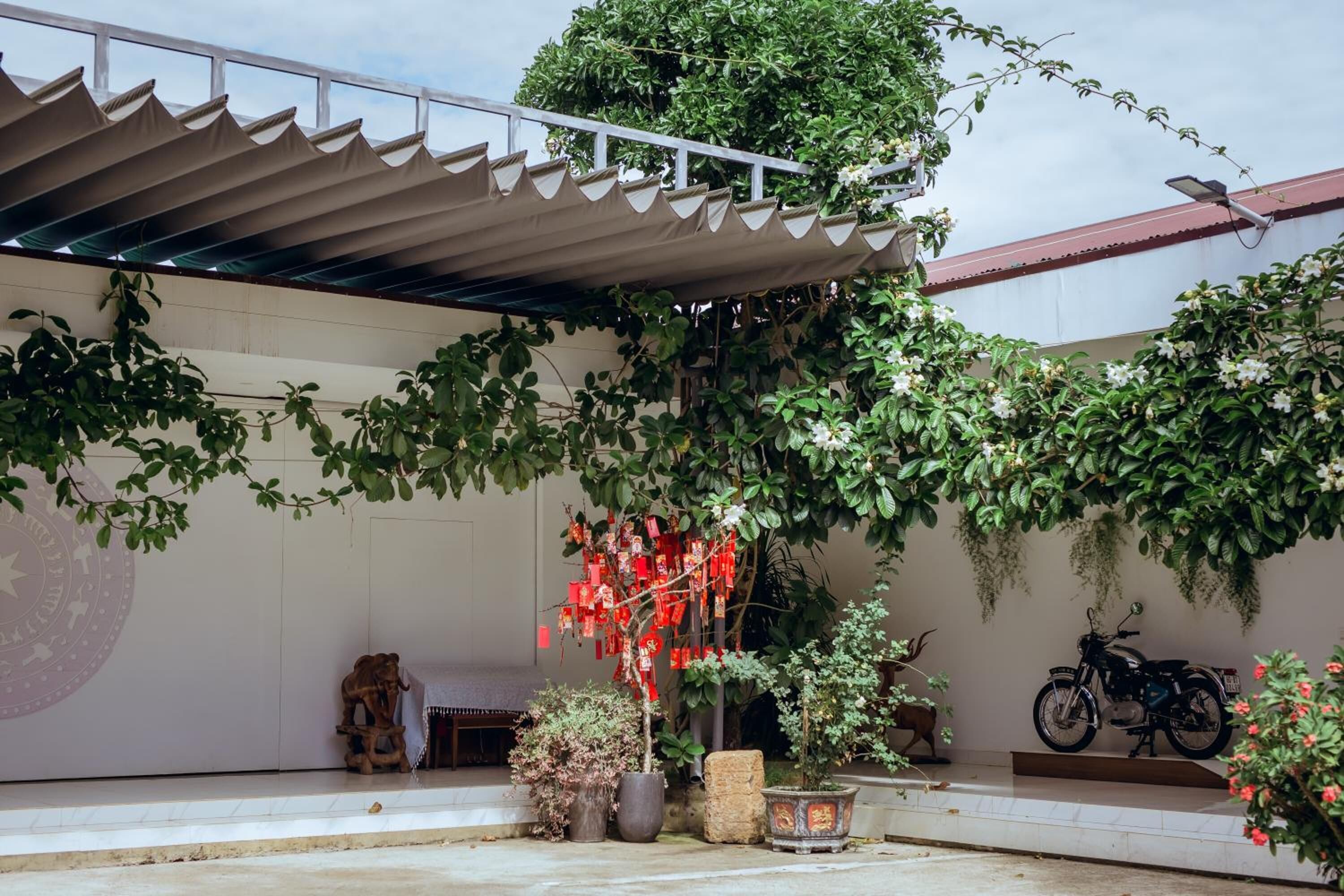 A covered outdoor area with a motorcycle parked, potted plants, and a decorative wall with a circular emblem.