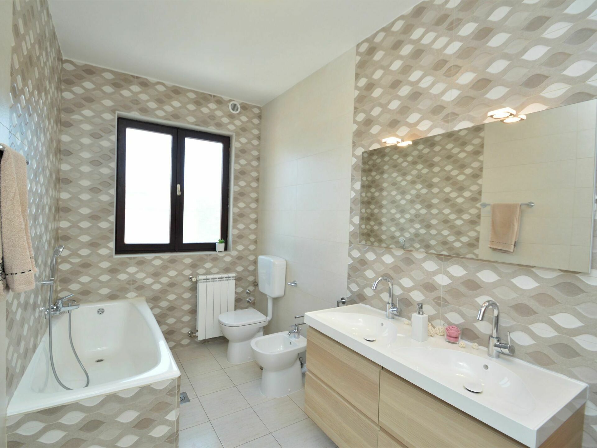 Een moderne badkamer met een badkuip, een wastafel met twee kommen, een toilet en een groot raam.