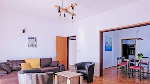 A modern living room with a sofa, a coffee table, and a chair. There is a dining area with a table and chairs. The room has wooden flooring and a large window. - Nice apartment for 7 people with A/C, hot tub, WIFI, TV and patio (Vinkuran)