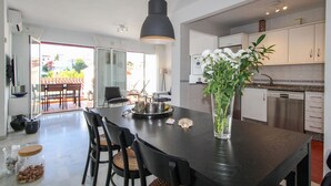 Una cocina moderna con armarios blancos, un comedor con una mesa y sillas negras, y un ventanal con vistas a un jardín.