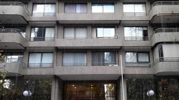Een meerlaags gebouw met een centrale ingang, balkons op elke verdieping en een kleine tuin ervoor.