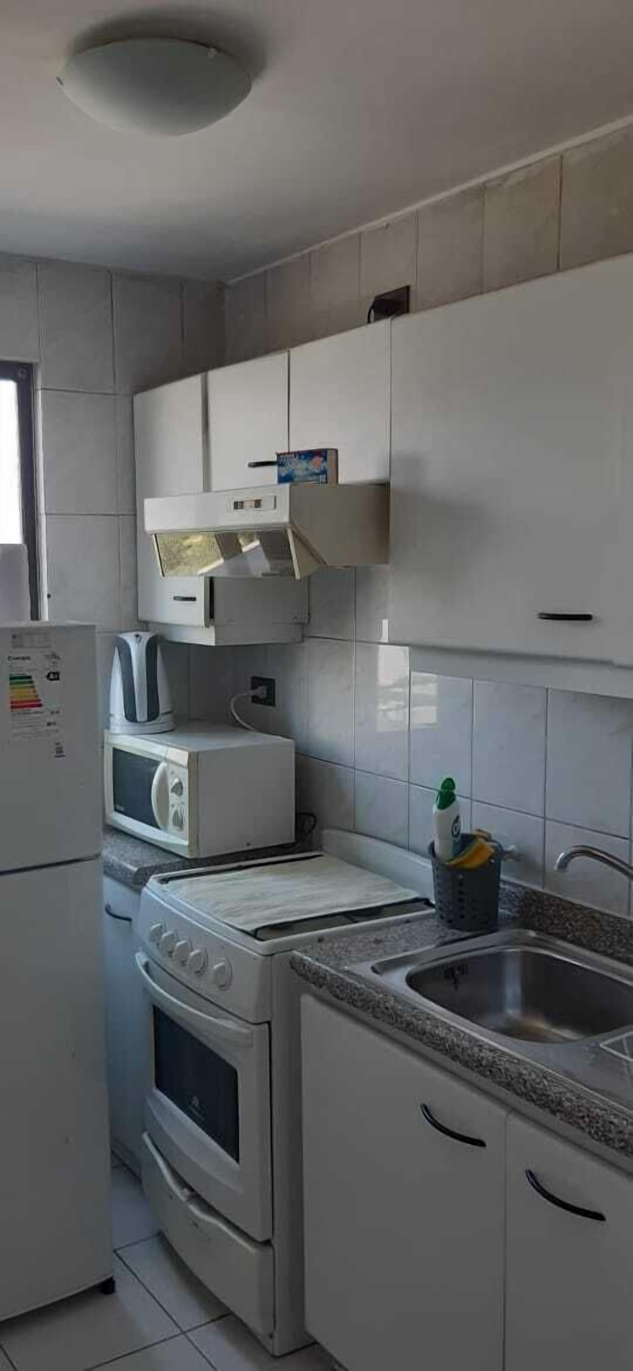 A compact kitchen with white cabinets, a microwave, a stove, and a sink.