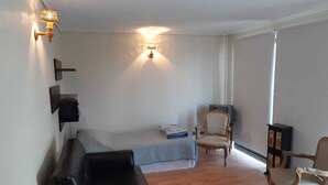 Een kamer met een bed, een zwarte bank, een houten stoel, een kleine tafel en wandlampen.