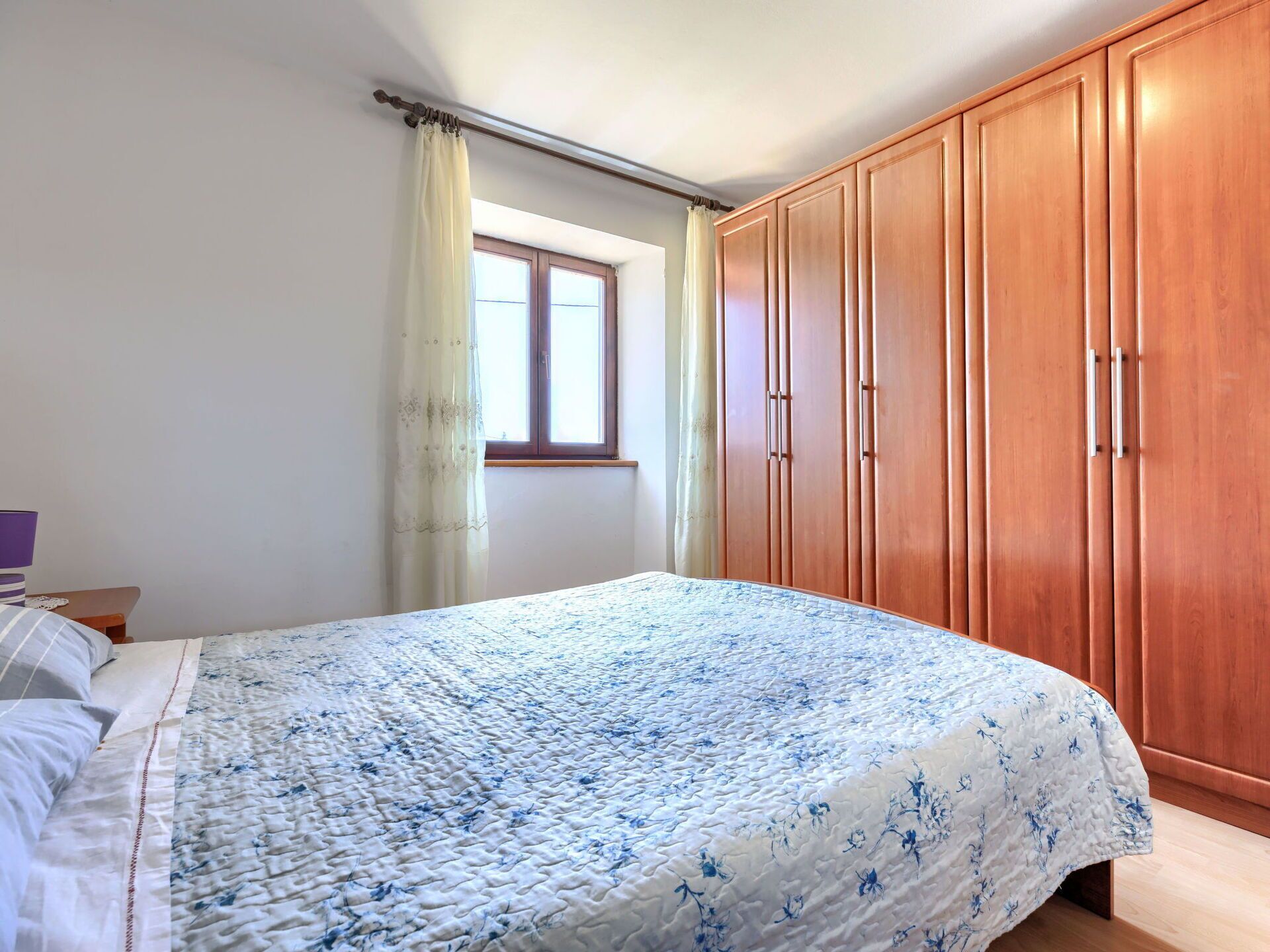 Une chambre avec un grand lit, une armoire en bois et une fenêtre avec des rideaux.