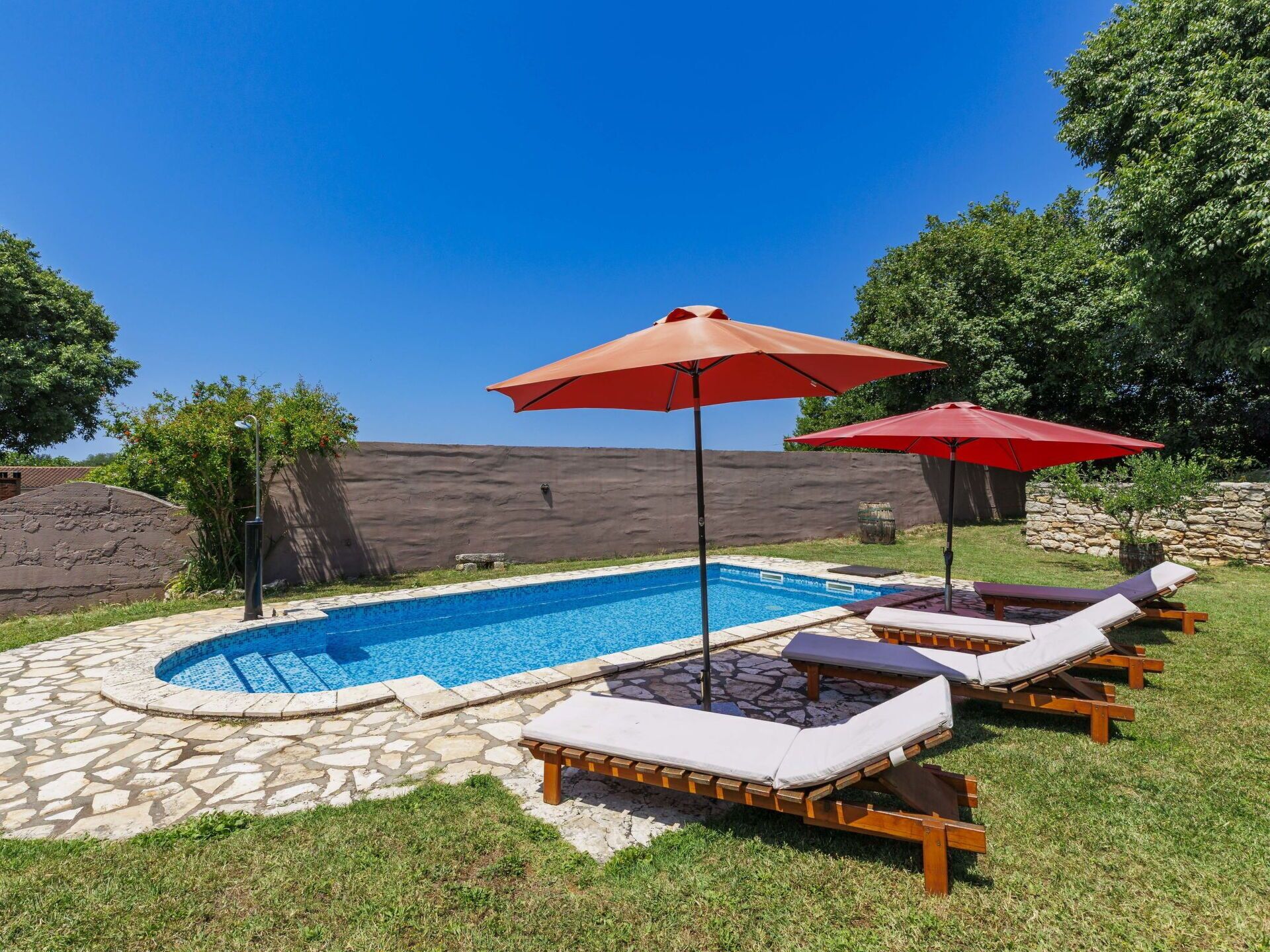 A swimming pool with lounge chairs and umbrellas, surrounded by stone tiles and greenery.