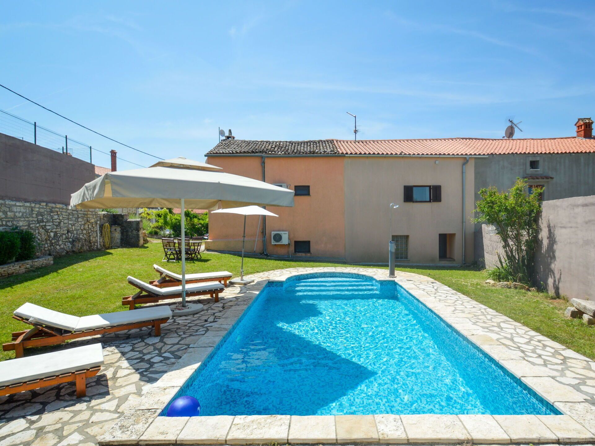 Piscina retangular com borda de pedra, rodeada por espreguiçadeiras e guarda-sóis.