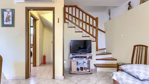 Una sala de estar con televisión, sofá, escalera de madera y una puerta que da a otra habitación.
