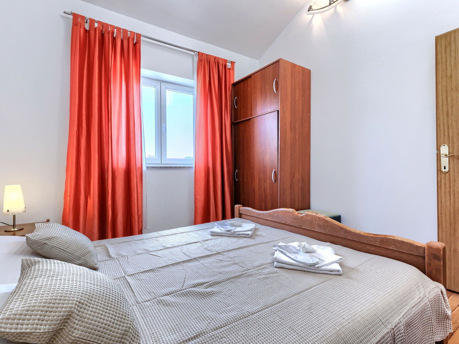 A bedroom with a bed, a wardrobe, a window with curtains, and a bedside lamp.