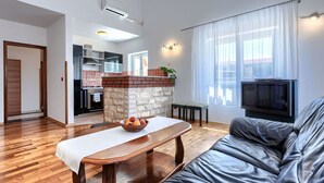 Un salon moderne avec un canapé en cuir, un banc en bois, un téléviseur et une cuisine en arrière-plan.