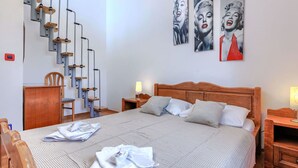 Une chambre à coucher comprenant un lit, une tête de lit en bois, une table de chevet, une lampe, une chaise, un bureau et un escalier avec une rampe.