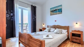 Une chambre à coucher avec un lit en bois, deux tables de chevet, une vue sur l’extérieur grâce à une porte coulissante, et un tableau accroché au mur.