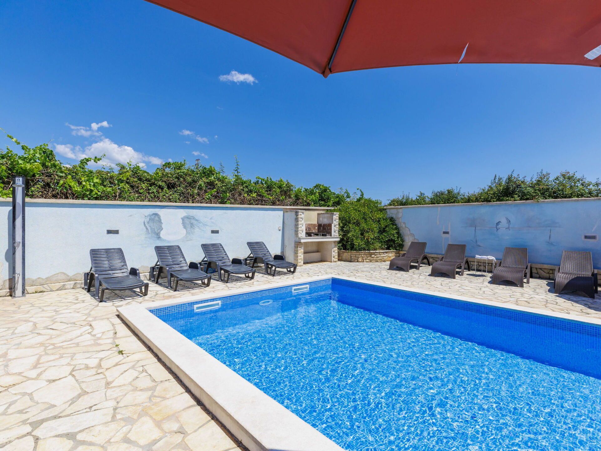 Une piscine avec des chaises longues et un espace barbecue.