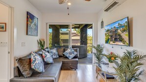 Una sala moderna con un sofá seccional, una mesa de centro de vidrio y vistas a un barrio residencial a través de amplios ventanales.