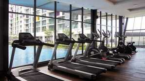 Gimnasio con cintas de correr y elípticas, ventanas amplias y vista a un edificio y agua.