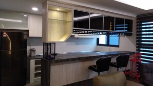 Una cocina moderna con una isla integrada, sillas negras y un taburete rojo.
