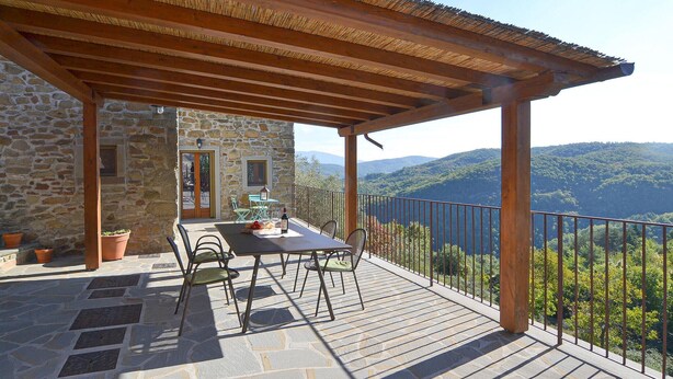 Un bâtiment en pierre doté d’une terrasse avec une pergola en bois.