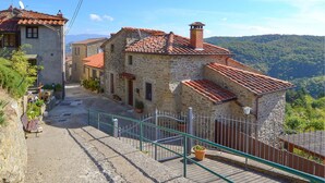 Un bâtiment en pierre avec un toit recouvert de tuiles rouges, un escalier menant à l’étage supérieur et une vue sur un paysage vallonné.