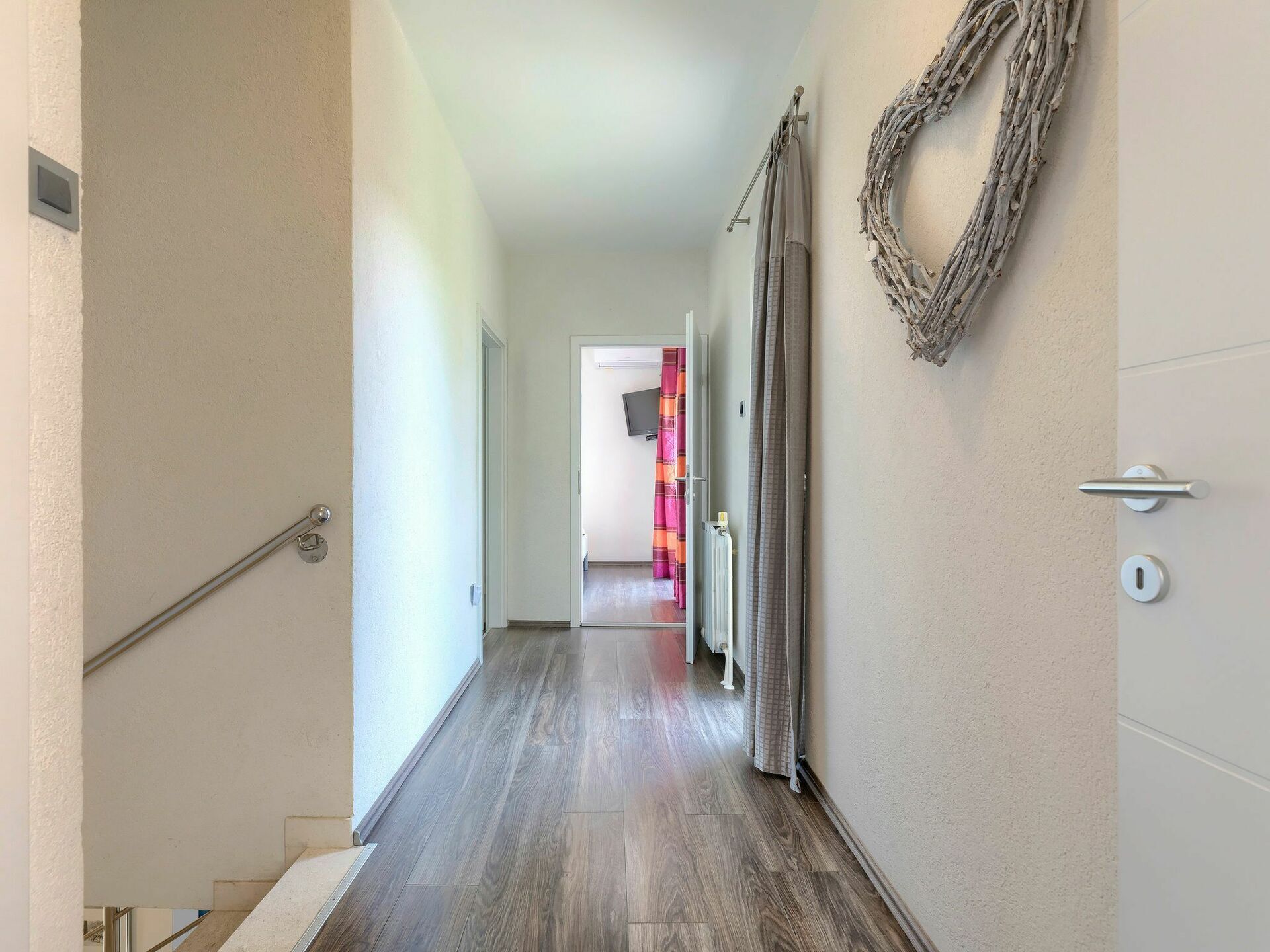 Ein Flur mit Holzboden, einer Handlauf links, einer Tür rechts und einem an der Wand befestigten Kranz.