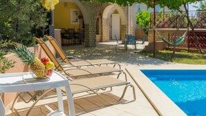 Un espace aménagé au bord de la piscine, avec des chaises longues, une table garnie de fruits et un hamac.