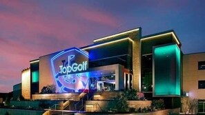 Um edifício moderno com um letreiro de neon chamativo que diz 'TopGolf'.