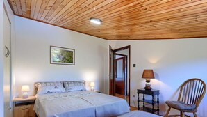 Un dormitorio con dos camas, techo de madera, lámparas de noche, una silla y una puerta que da a otra habitación.
