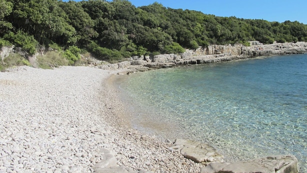 Una playa de guijarros con agua cristalina y afloramientos rocosos.
