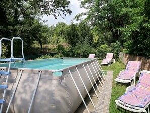 An above-ground swimming pool with a ladder, surrounded by grass and trees.