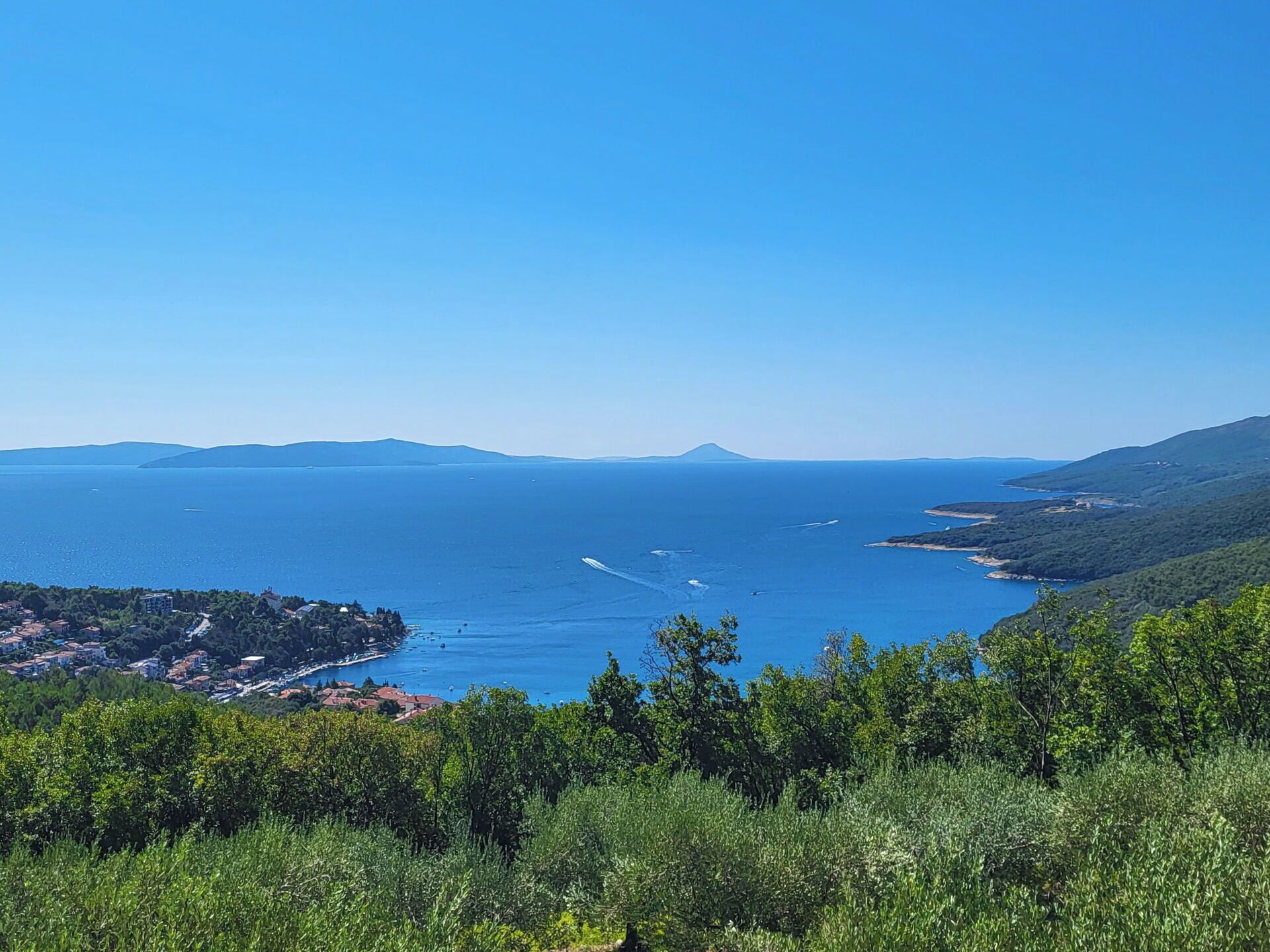 Eine Küstenlandschaft mit freiem Blick auf das Meer, Hügel und eine kleine Stadt mit Gebäuden.