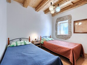 A bedroom with two beds, a stone wall, a window, and wooden ceiling beams.