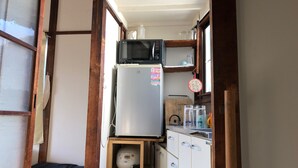 Una cocina compacta con refrigerador, microondas y un estante con frascos y hervidor.