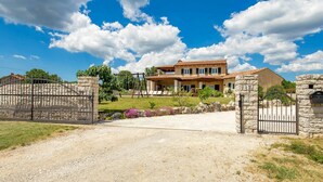 Une maison à deux étages avec une allée en gravier menant à une entrée fermée par un portail.