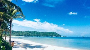 Una playa de arena blanca, palmeras y un cielo azul despejado.
