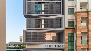 Un hotel de varios pisos con diseño moderno, que destaca por una entrada principal con escaleras y un cartel que dice “THE TIME”.
