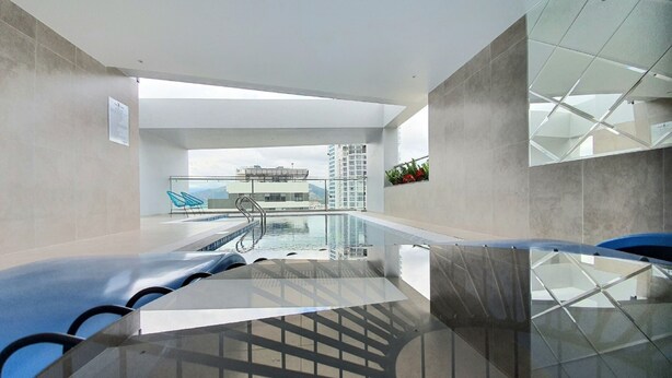 Una piscina interior moderna con paredes de vidrio transparente, una silla azul y vistas a un edificio de gran altura.