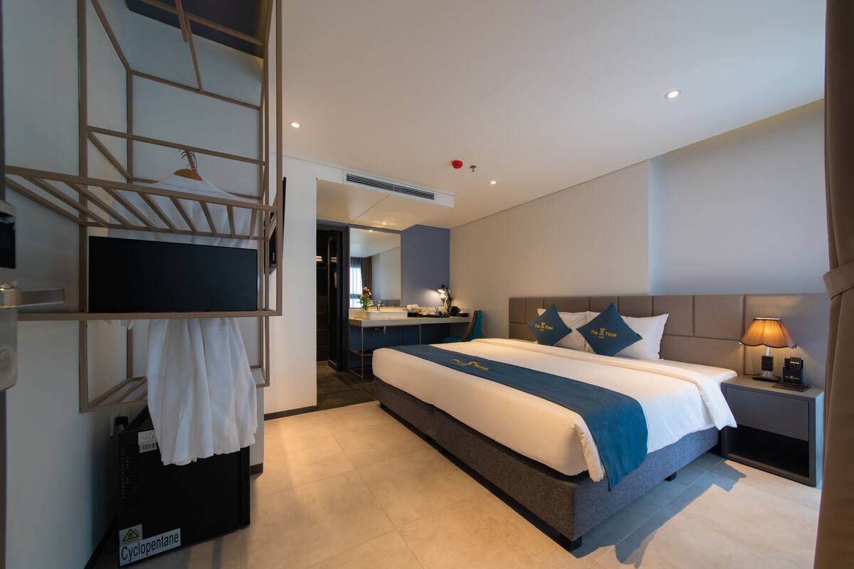 A modern hotel room with a large bed, a desk, and a bathroom visible through an open door.