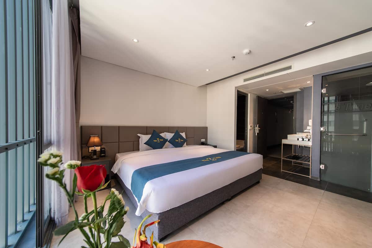 A hotel room with a large bed, a bedside table with a lamp, a mirror, and a view of the hallway.