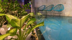 An indoor pool area with a glass wall, potted plants, and two blue chairs. - The Time Hotel Nha Trang (Nha Trang)