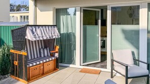 A patio with a covered seating area, a sliding glass door leading to a kitchen, and a white chair. - 1 bedroom stunning apartment in Graal Müritz (Graal Müritz)