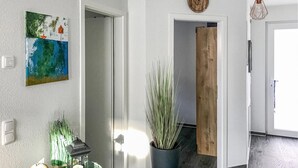 A hallway with a painting, a potted plant, a wooden door, and a hanging light fixture. - 1 bedroom stunning apartment in Graal Müritz (Graal Müritz)