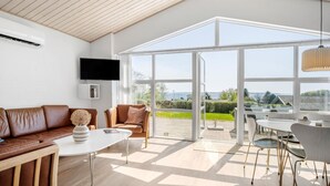 Ein modernes Wohnzimmer mit einem großen Glasfenster zum Außenbereich, einem flachbildfernseher an der Wand und einer Sitzecke mit Ledersofas und einem Couchtisch.