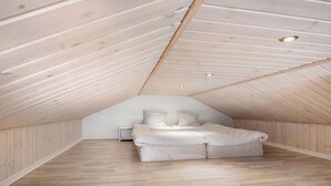 Ein kleines Schlafzimmer im Dachgeschoss mit schrägem Dach, einem Bett und einer weißen Wand.